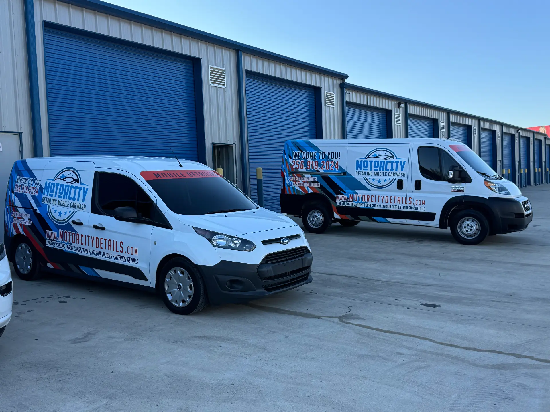 Two wrapped Motorcity Detailing mobile units parked outside the shop